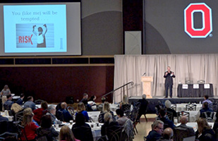 Image of a man standing on a stage addressing an audience of people at a conference